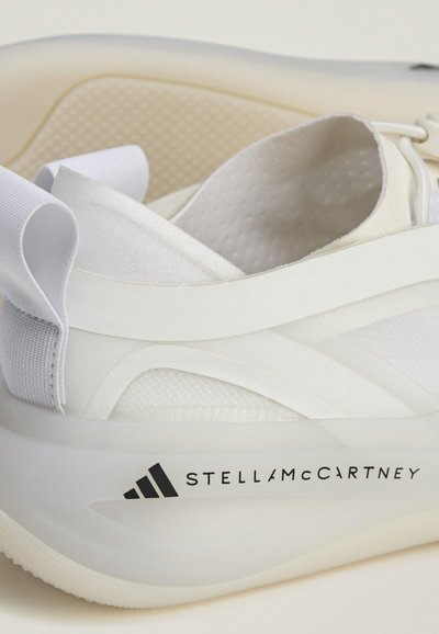 Fehér sportcipő, amely többféle textúrájú felsőrésszel rendelkezik, szaténból és hálóból készült, áttetsző talppal és fekete kontrasztos márkajelzéssel.