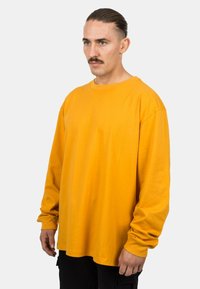 Langärmliges T-Shirt aus leuchtend gelbem Baumwollstoff. Verfügt über einen runden Ausschnitt, einen lockeren Schnitt und überschnittene Schulternähte. Keine sichtbaren Muster oder Akzente.