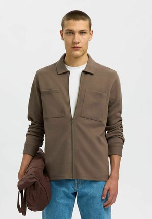 Brown zip-up jacket with two chest pockets, soft texture, and a flat collar, paired with light blue jeans and a brown bag.