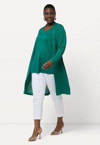 Turkusowy długi kardigan na turkusowej bluzce, w połączeniu z białymi wąskimi spodniami i cielistymi sandałami na obcasie. Gładki materiał, z otwartym przodem i długimi rękawami.