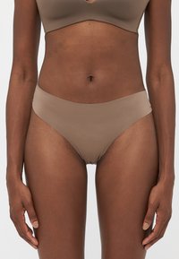 Woman wearing matching beige seamless bra and bikini-cut underwear against a plain white background.