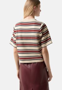 Striped t-shirt in beige, red, and navy, with a cropped design and short sleeves. Fabric appears soft with a smooth texture.