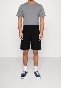 Harmaa lyhythihainen t-paita, mustat shortsit, valkoiset nilkkasukat ja moniväriset lenkkitossut. Puuvillamateriaalia ja klassinen istuvuus.