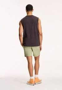 Tmavě šedé tílko, světle zelené šortky, oranžové vysoké tenisky. Hladká tkanina, pravidelný střih, jednoduchý design, bez viditelných log.