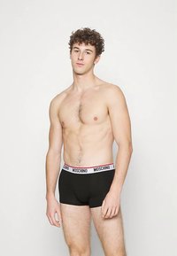 Cuecas boxer pretas com cintura elástica branca e vermelha com o logótipo "Moschino". O material parece suave com um design ajustado.