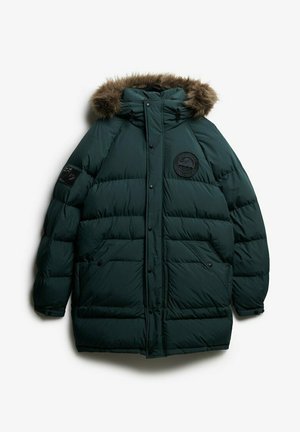 Mørkegrønne pufferjakke med hætte med pelskant. Har et rundt logo-patch på brystet og trykknaplukninger. Blødt materiale og isoleret design.