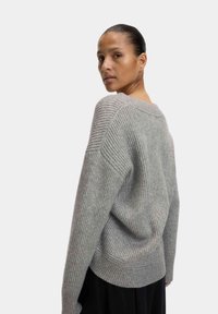 Grau gestrickter Pullover mit lockerem Schnitt, weiten Ärmeln und strukturiertem Oberflächendesign. Mit Rundhalsausschnitt und überschnittenen Schultern.