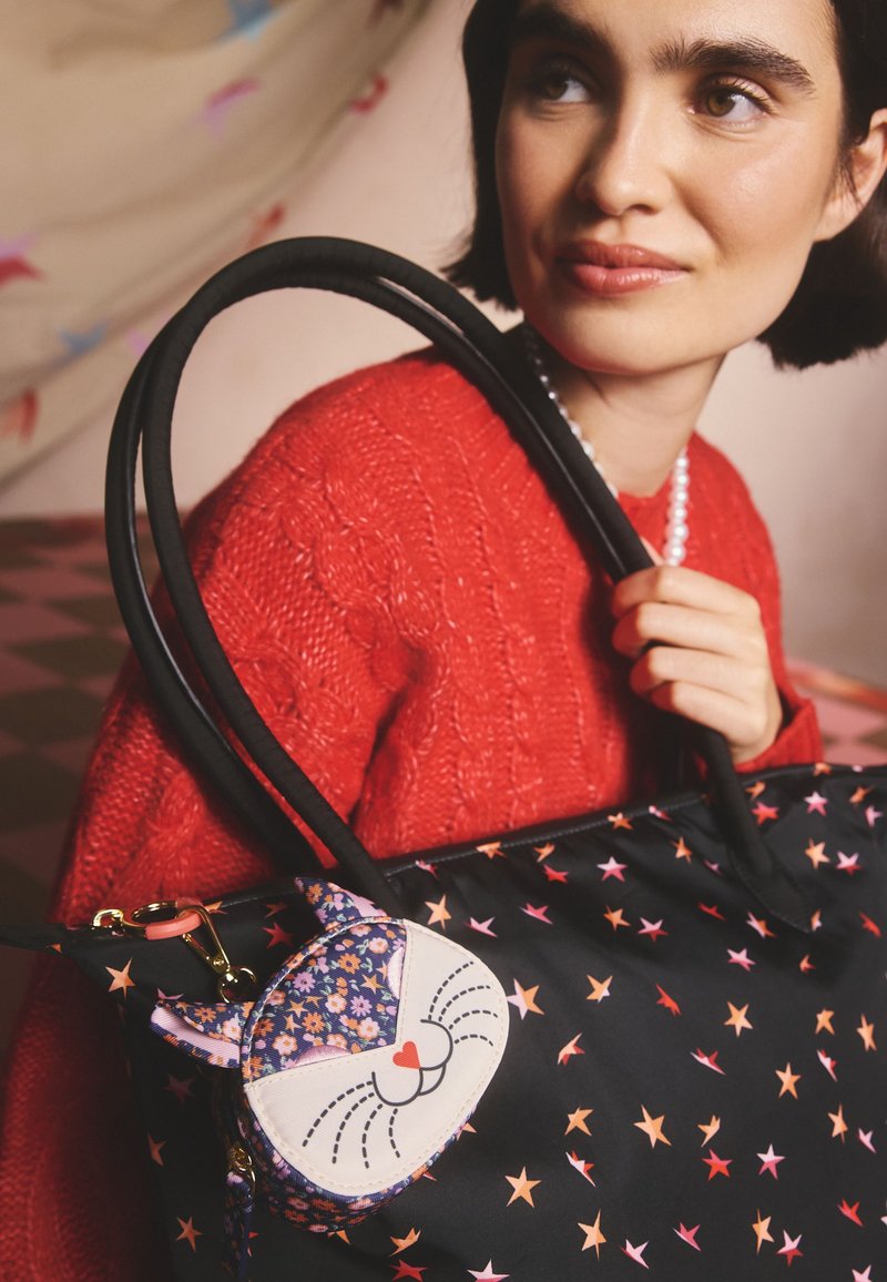 Svart tygväska med mönster av stjärnor i flera färger, utrustad med en avtagbar kattformad necessär med blommönster och en hjärtformad näsa.