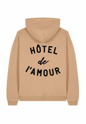 Beige hoodie met capuchon, voorzien van zwarte tekst "HÔTEL de l’amour" in een gebogen lay-out op de achterkant. Zachte textuur en standaard pasvorm.