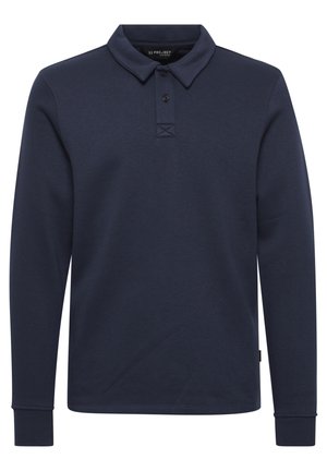 Temno modra polo s dolgimi rokavi, izdelana iz mehke tkanine. Ima ovratnik, placket s tremi gumbi in rebraste manšete. Diskretna oznaka s logotipom na robu.