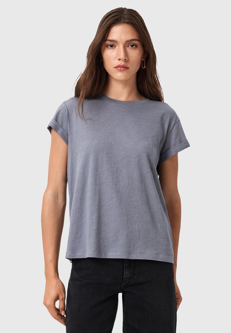 Camiseta gris de manga corta, de corte relajado, con cuello redondo, hecha de una tela suave con una textura sutil, combinada con pantalones negros.