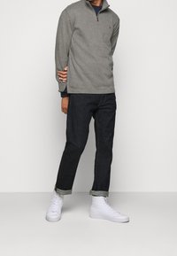 Grå kvartzip fleecepullover, mörka denimjeans och vita högskaftade sneakers. Notabel brun dragkedja och uppvikta jeans. Slät struktur.