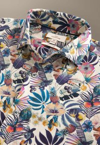 Chemise en lin de taille moyenne, boutonnée, avec un motif tropical multicolore de fleurs, feuilles et fruits, incluant des ananas et des fleurs d'hibiscus.