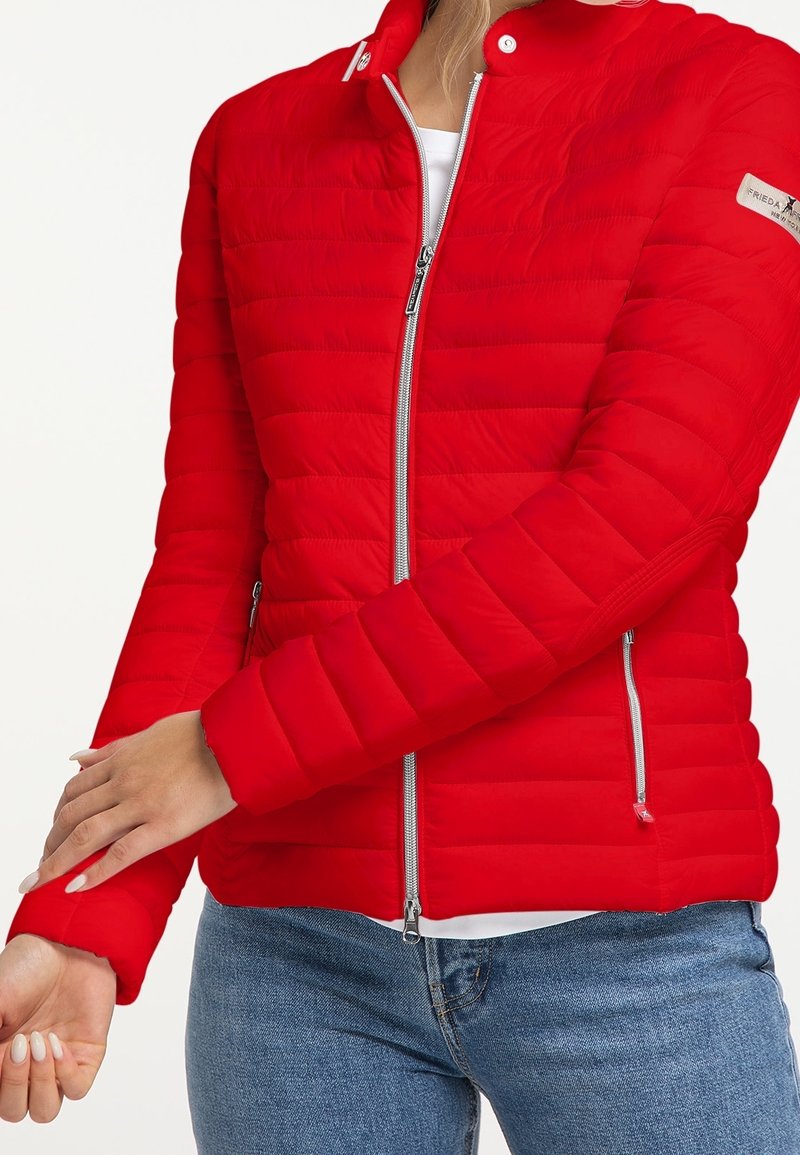 Červená prošívaná bunda s lehkým designem, vybavená stříbrnými zipy a cvočky a dvěma bočními kapsami. Zvýrazněná žebrovanými manžetami.