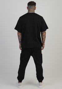 Černé bavlněné tričko s krátkými rukávy a volnějším střihem, doplněné černými cargovými kalhotami s bočními kapsami a elastickými manžetami.