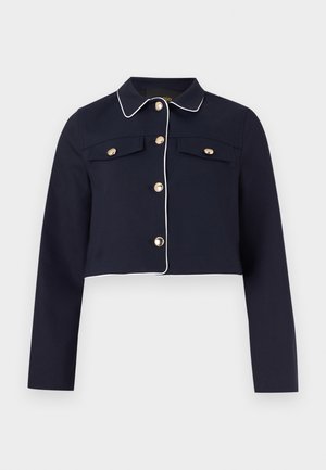 Veste courte bleu marine avec passepoil blanc, manches longues, fermetures à boutons dorés, et poches poitrine à rabat sur un fond uni.