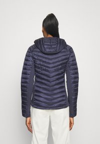 Marine blauwe pufferjack met een chevronquiltpatroon, een capuchon en aansluitende mouwen. Het materiaal lijkt soepel en lichtgewicht te zijn.