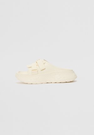 Sandal de slide de cor creme feito de borracha. Apresenta duas alças ajustáveis e uma sola texturizada com um padrão geométrico para melhor aderência.