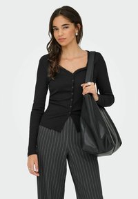 Czarny kardigan z dekoltem w serek, zapinany na guziki, z koronkowymi wykończeniami, w zestawieniu z czarno-szarymi spodniami w paski oraz czarną skórzaną torbą na ramię.