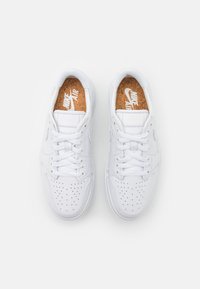 Bílé tenisky Nike Air s perforovanými špičkami, bílými tkaničkami a korkovými vložkami s logem Nike Air, z pohledu shora na bílém pozadí.