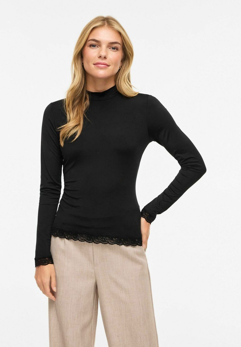 Svart langermet topp med høy hals, med blonderkant nederst og på ermene. Glatt stoff med en tettsittende silhuett.