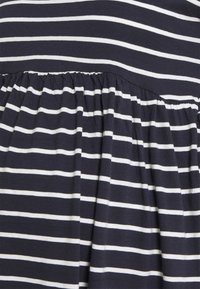 Detailní záběr na tmavě modrou tkaninu s pravidelně rozmístěnými bílými vodorovnými pruhy a nařaseným stehem vytvářejícím sklady.