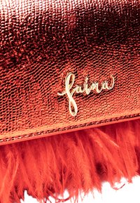 Borsa a tracolla rossa con texture, caratterizzata da un logo dorato e vivaci dettagli di piume rosse alla base. Superficie liscia con dettagli di pattern distintivi.