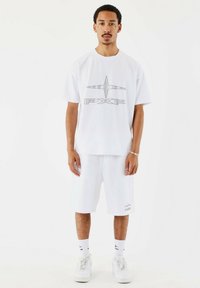 Witte T-shirt met korte mouwen en een zilveren logo, gecombineerd met witte shorts. Inclusief witte sokken en witte sneakers. Glad stof en een comfortabele pasvorm.