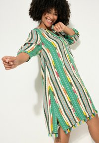 Multicolor jurk met een groene basis en verticale strepen in roze, geel en zwart, voorzien van een franjerand en korte mouwen.