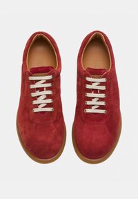 Sneaker in suede rosso con lacci beige, punta rotonda e finitura texture. Le suole in gomma offrono un accento marrone a contrasto.