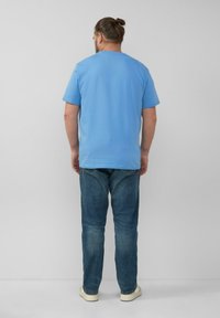 Blauwe katoenen T-shirt met korte mouwen, ronde halslijn en een relaxed fit, gecombineerd met donkerblauwe spijkerbroek en lichtgekleurde schoenen.