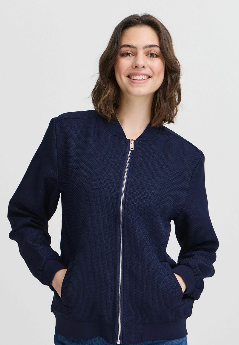Giacca bomber navy con un motivo testurizzato, chiusura con zip, polsini a costine e tasche laterali. Realizzata in materiale leggero.