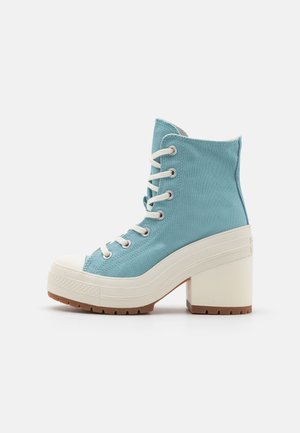 High-top sneaker van lichtblauw canvas met witte veters, een witte rubberen neuskap en een stevige beige blokhak. Gestructureerde rubberen zool.