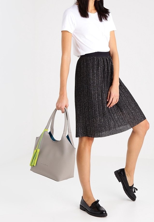 Szara torebka o fakturze, ozdobiona neonowożółtymi frędzlami, połączona z białą koszulką i czarną plisowaną spódnicą oraz czarnymi butami.