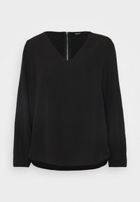 Blouse noire à manches longues avec encolure en V et fermeture éclair au dos, présentant une texture lisse et une coupe décontractée. Sans motifs ni accents.