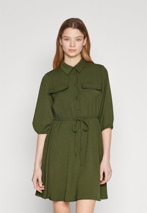 Robe vert olive avec un devant à boutons, deux poches poitrine et une taille élastique. Présente des manches courtes bouffantes et une texture douce.