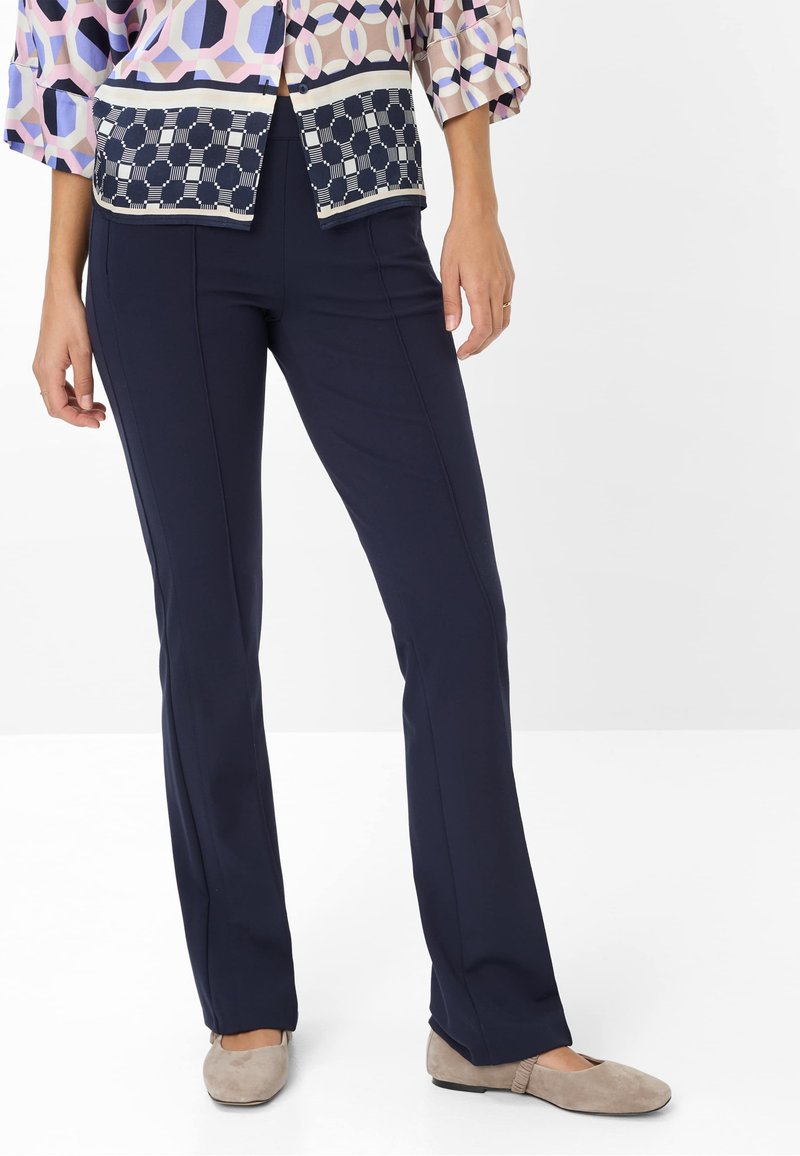 Marineblauwe stretchbroek met een slim fit, voorzien van voornaad en een gladde textuur. Gekleed met een geblokte blouse en neutrale flats.