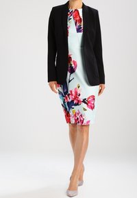 Black blazer over a fitted, light blue floral dress with pink and purple accents. Smooth fabric, knee-length design, paired with light gray heels.