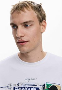 Valge puuvillane T-särk, millel on sinine, roheline ja must graafiline trükk. Ümar kaelus ja lühikesed varrukad. Minimalistlik tekstuur, juhuslik sobivus.