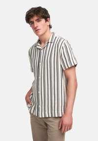 Korte mouw knoopshirt met verticale marineblauwe en crèmekleurige strepen, een camp-kraag en een gestructureerde stof. Ggedragen met kaki broek.