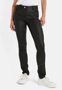 Pantalones de imitación de cuero negros con un ajuste slim, que cuentan con bolsillos frontales y sutiles tachuelas en los lados. Combinados con zapatillas blancas con cordones.