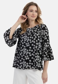 Top nero fluido con stampa di margherite bianche, scollatura rotonda e maniche a campana svasate. Realizzato in tessuto leggero, presenta una texture arricciata sulle maniche.