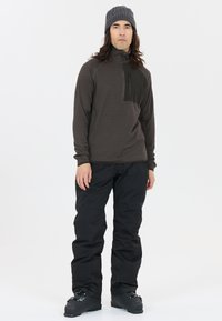 Brun långärmad tröja med en svart dragkedjeficka på bröstet, tillsammans med svarta snöbyxor och en grå stickad mössa. Slät tygtextur.