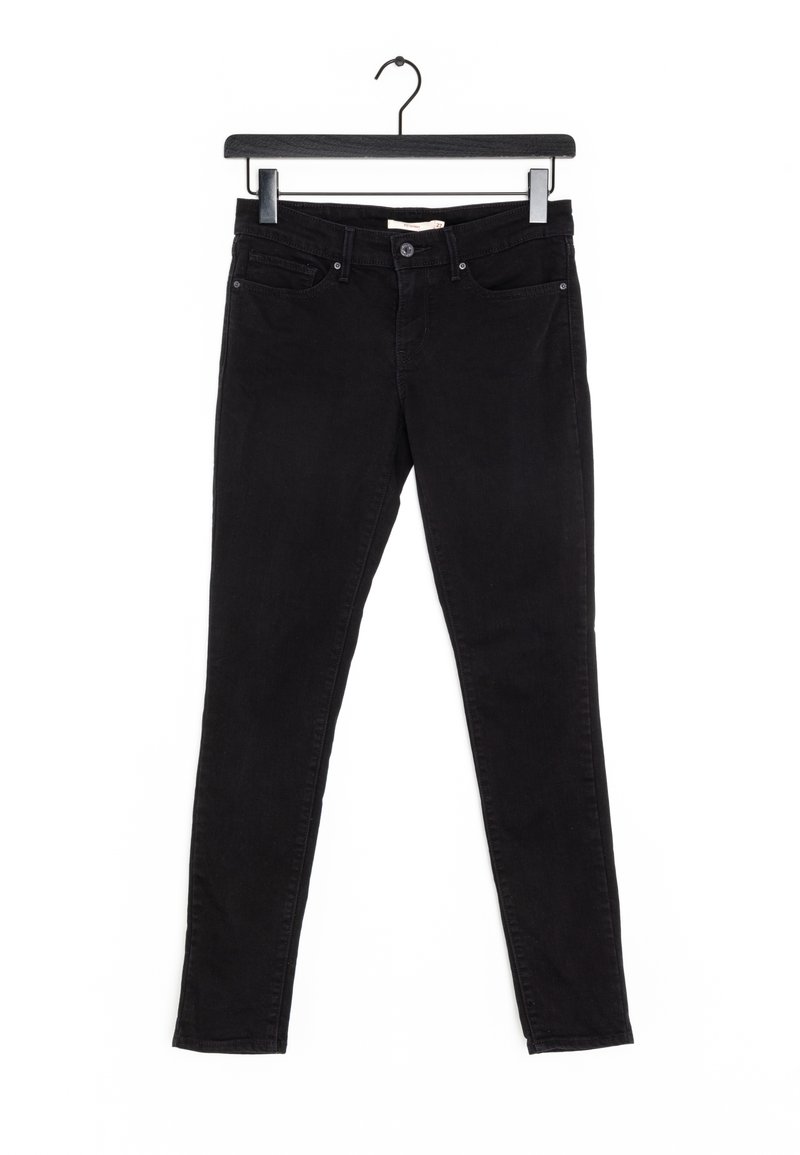 Jean noir slim avec poches avant accroché à un cintre en bois noir sur fond blanc.