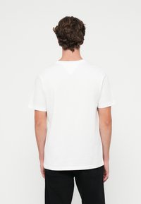 Hvid T-shirt med korte ærmer, rund halsudskæring og en trekantet detalje på ryggen. Blødt stof, afslappet pasform og lige kant.