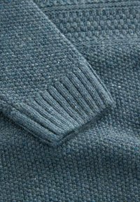 Maglione lavorato a maglia in verde scuro con un motivo texturizzato. Presenta polsini a coste e un tessuto spesso e liscio. Aspetto morbido e caldo.