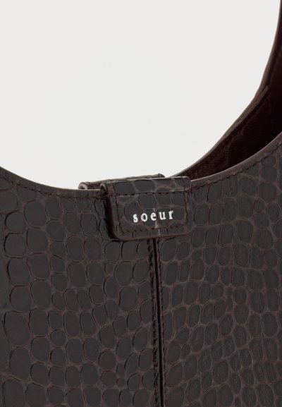 Σκούρα καφέ τσάντα χειρός με υφή μοτίβου δέρματος ερπετού και μια μικρή ετικέτα με την ένδειξη «soeur» κοντά στη πάνω ραφή.