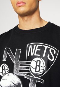 Felpa nera in cotone con collo rotondo, caratterizzata da una grande grafica "NETS" con motivi legati al basket in bianco. Il design ha un aspetto testurizzato e usurato.