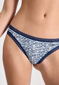 Slip blu navy e bianchi con un tessuto strutturato e un bordo in pizzo attorno alla vita, evidenziando un design a stampa geometrica.