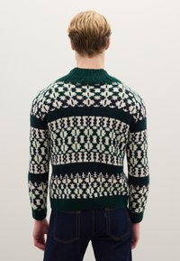 Grüner Wollpullover mit weißen und marineblauen geometrischen Mustern, einem gerippten Rundhalsausschnitt und eng anliegenden Ärmeln. Texturiertes Strickgewebe.